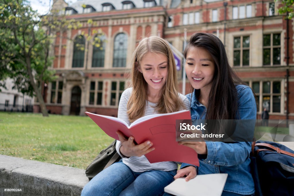 Happy female students studying outdoors reading notes on a notebook - education concepts